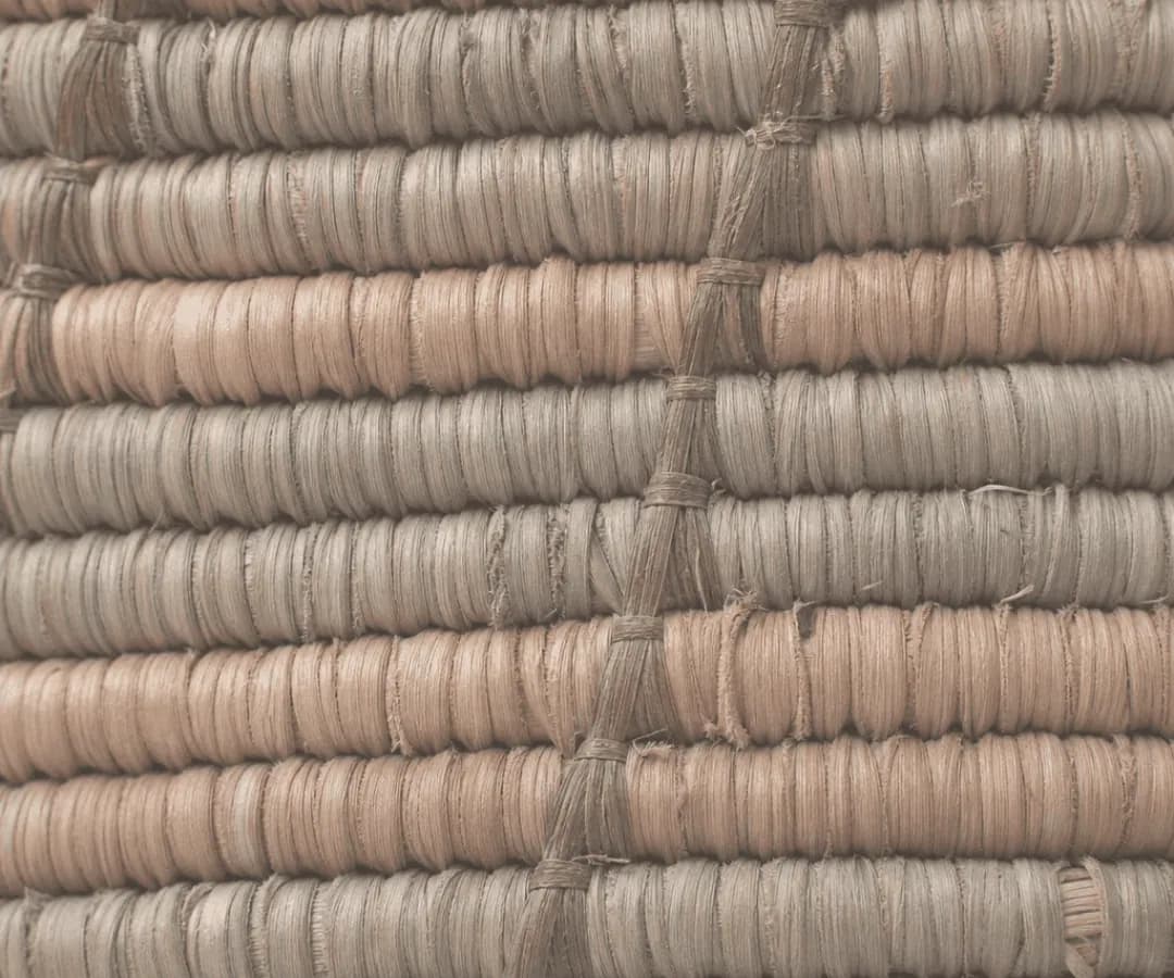 Coiled rows of raffia in dusty pink and grey, bound with a twisted cord