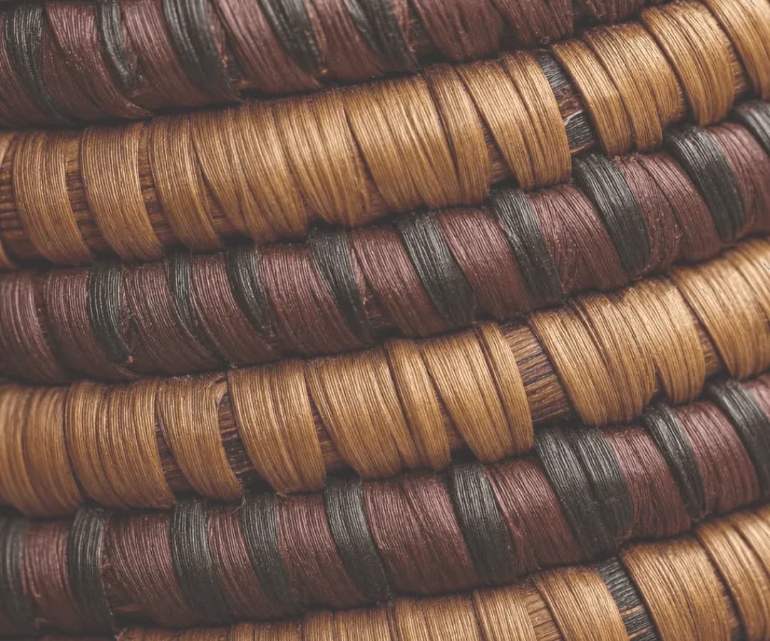 Coiled basketry rows in caramel, maroon and black fibres