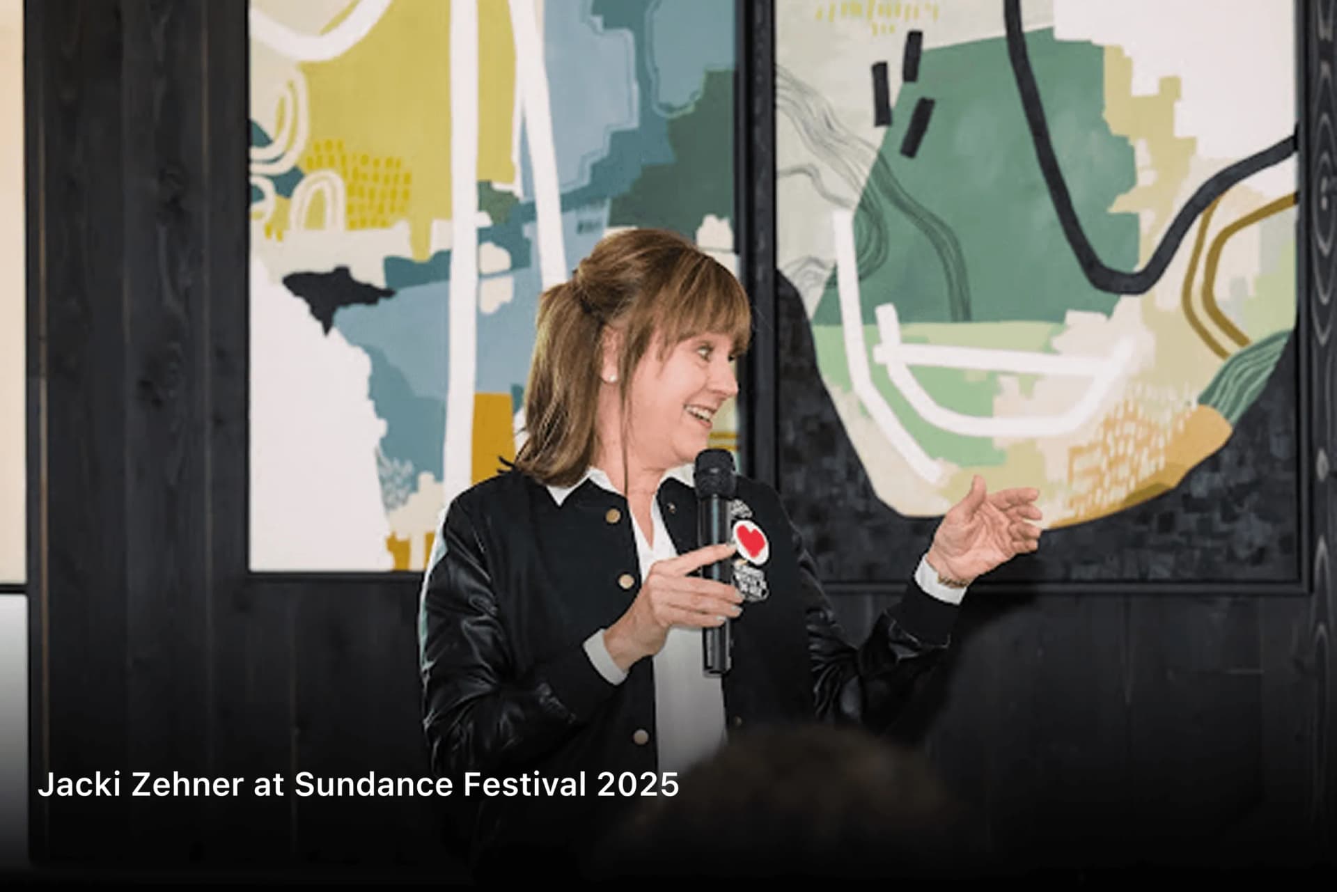 Jacki Zehner speaking into a microphone in front of an abstract mural at Sundance Festival 2025