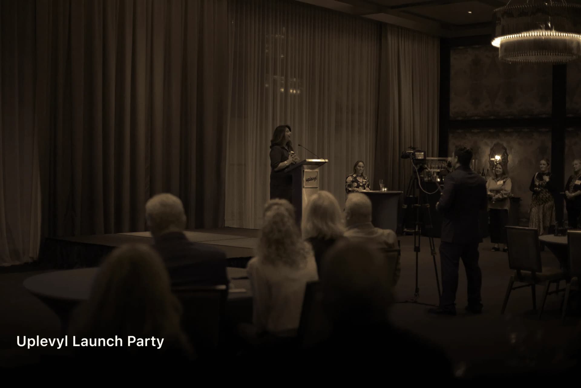 Guests seated in a dim ballroom facing a speaker at the Uplevyl launch party